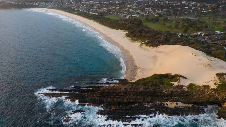 A coastal town with a sandy beach, rocky coastline, and residential areas.