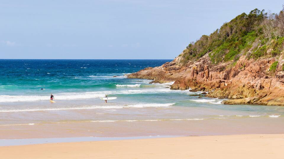A beach with clear blue water, a sandy shore, and rocky cliffs.