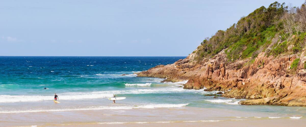 A beach with clear blue water, a sandy shore, and rocky cliffs.