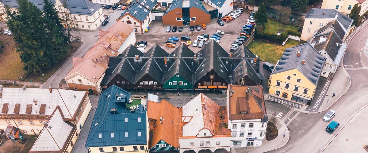 An aerial view of a town with a central market area, surrounded by various buildings and parked cars.