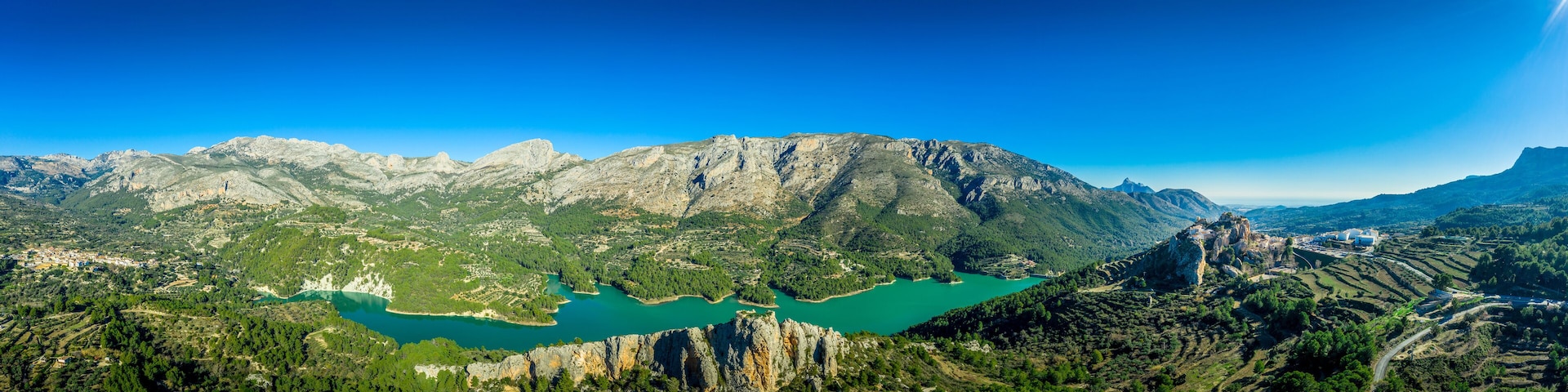 Un paisaje montañoso con un lago turquesa y un pequeño pueblo.