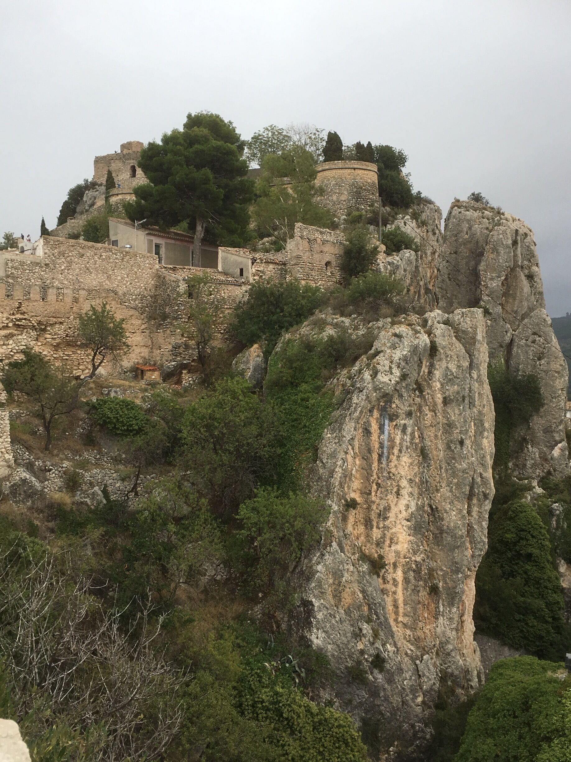 A historic stone fortress atop a rocky hill with surrounding greenery.