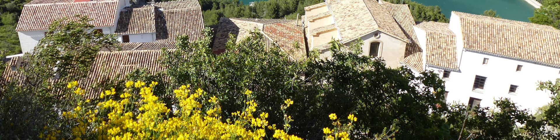 A mountainous landscape with a turquoise lake surrounded by greenery and buildings with terracotta roofs.