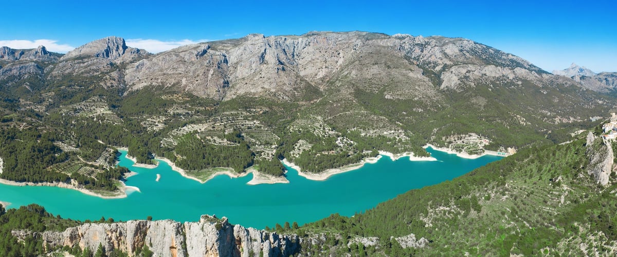 A turquoise lake surrounded by rugged mountains and dense forests.