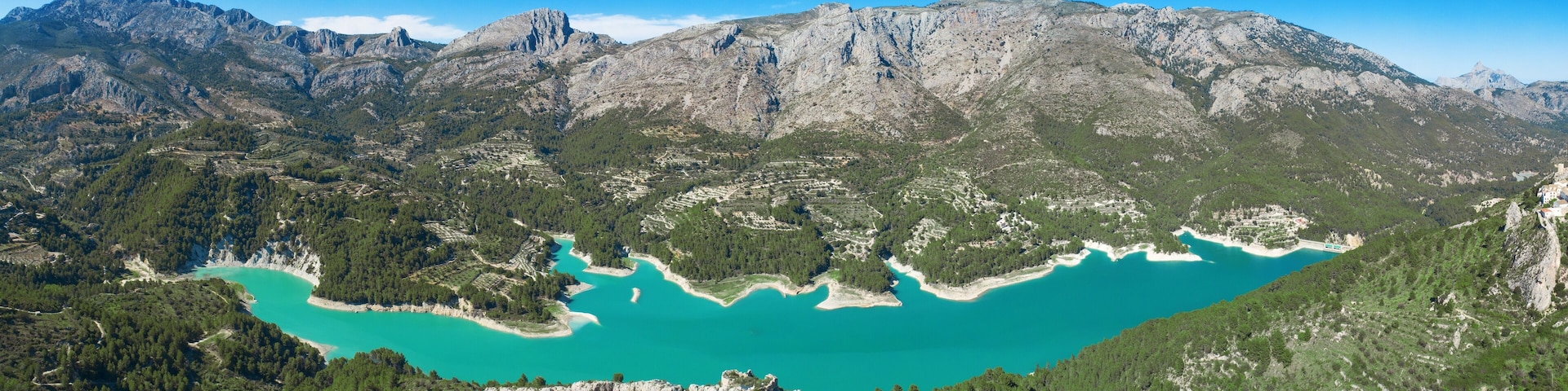 A turquoise lake surrounded by rugged mountains and dense forests.