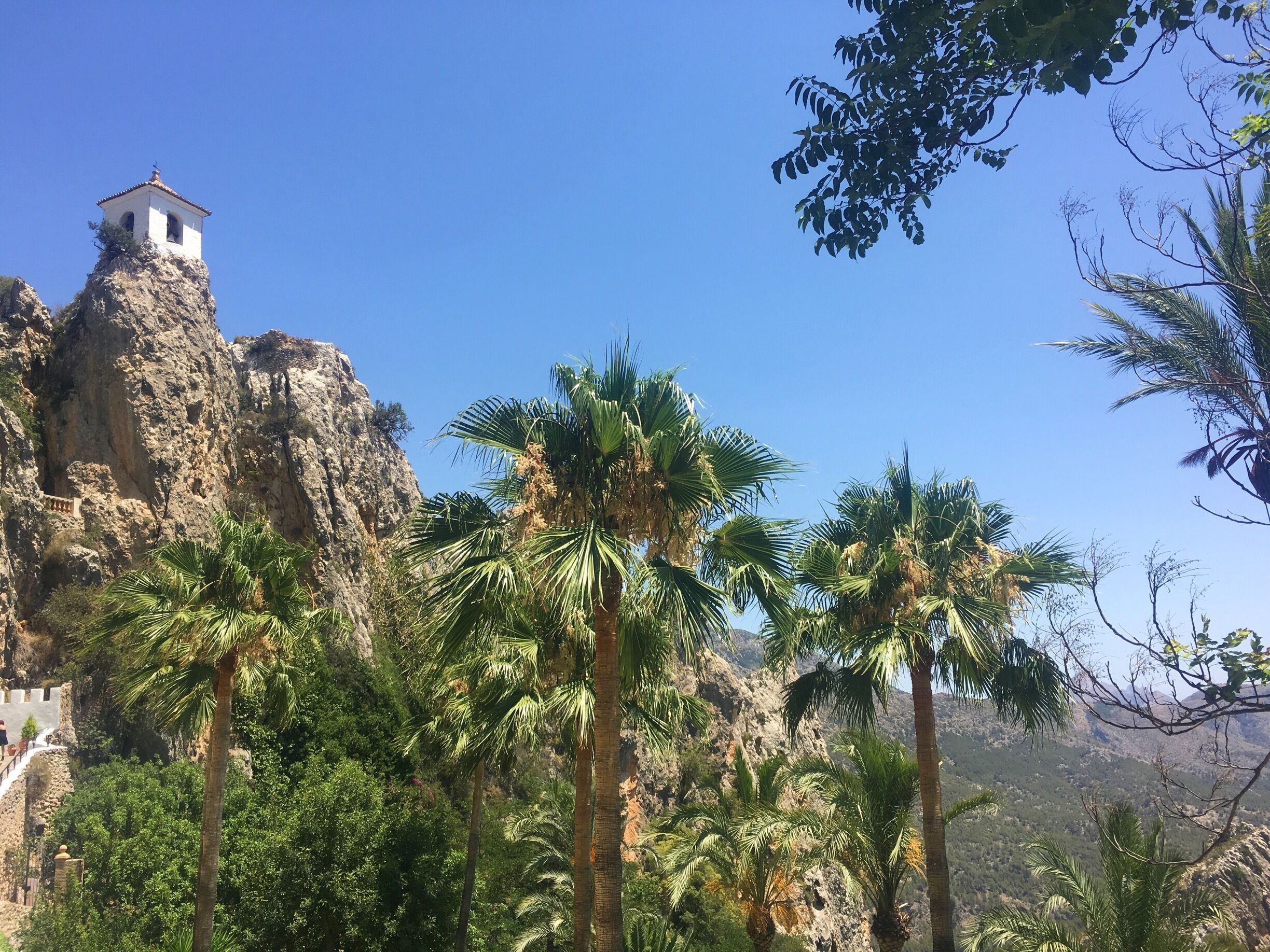 A rocky mountain with a bell tower and palm trees.