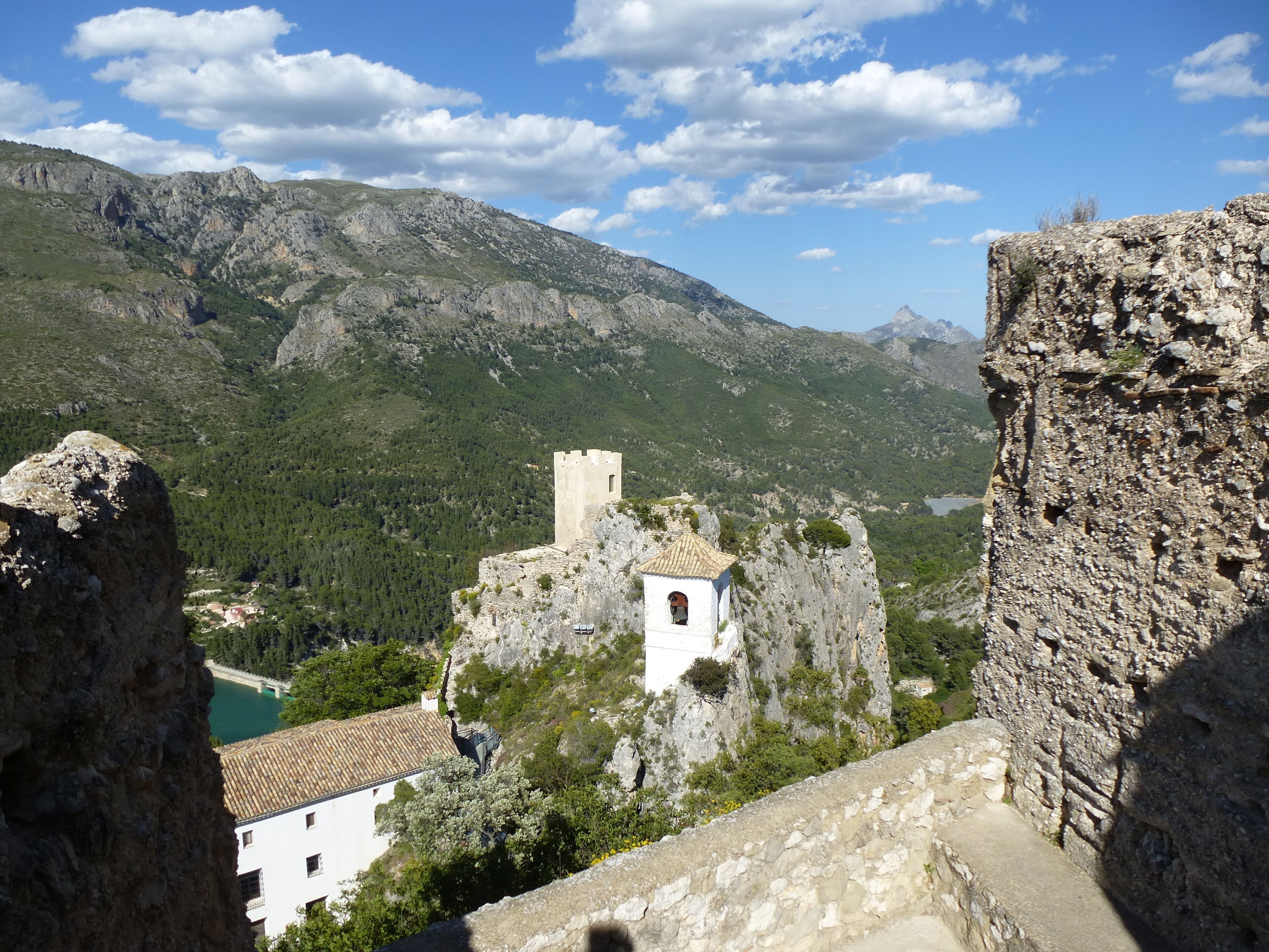 A mountainous landscape with a castle perched on a cliff overlooking a valley.