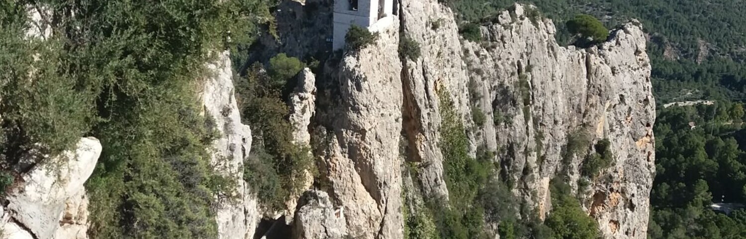 Uma igreja branca empoleirada em um penhasco rochoso, com montanhas ao fundo.