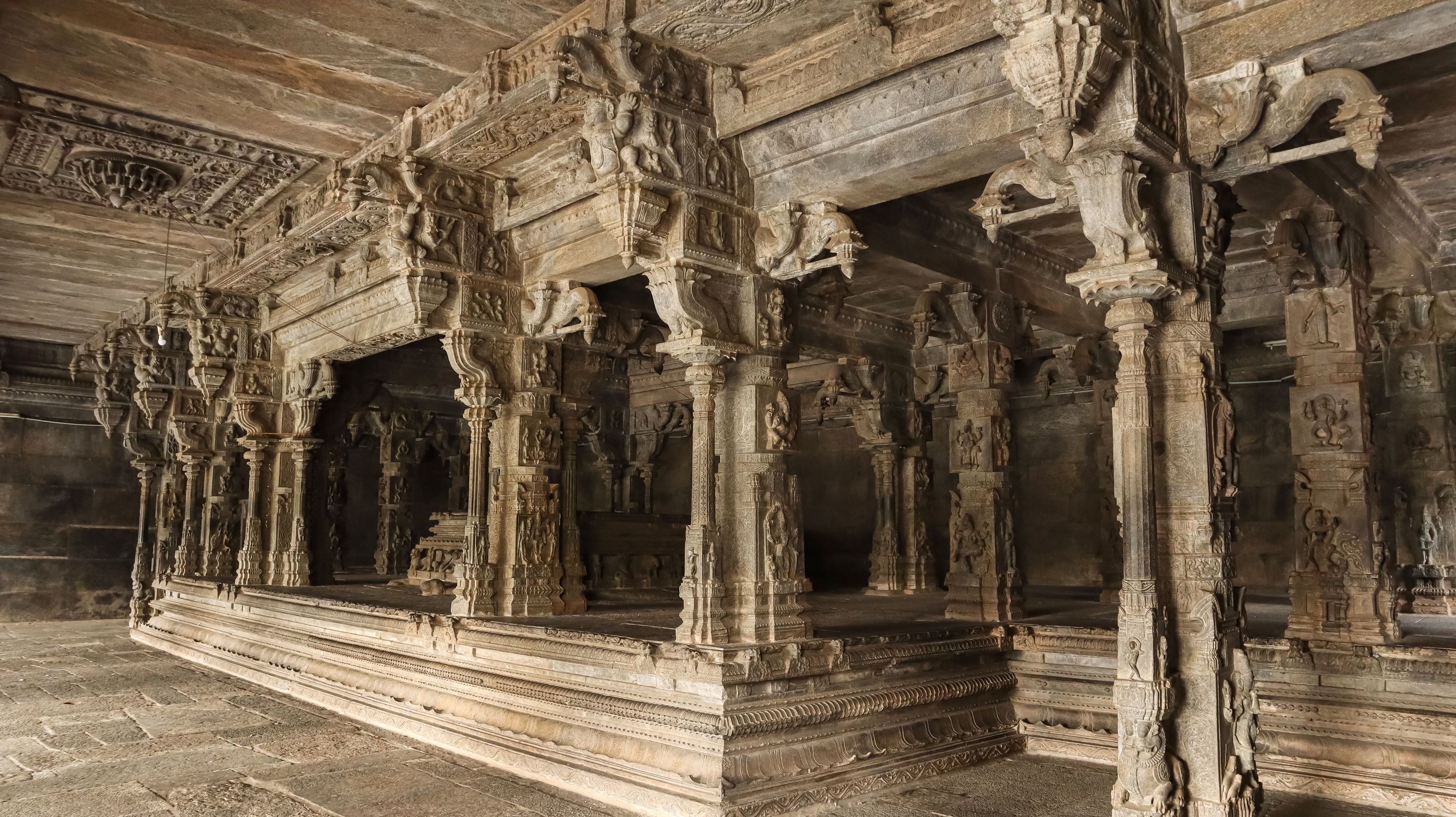 Aufwändig verzierte Steinsäulen und eine detaillierte Decke in einem antiken Tempel.