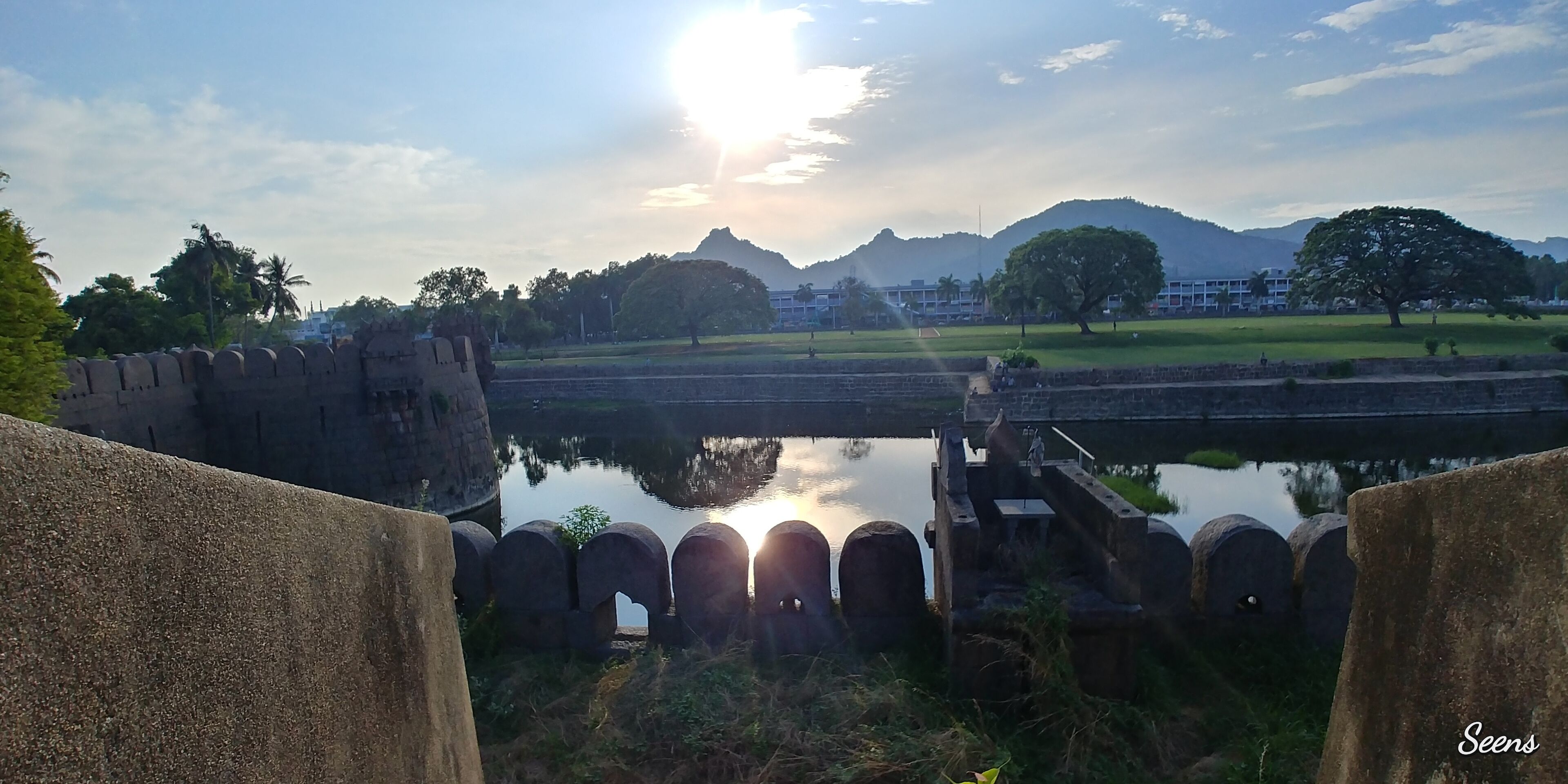 A historic fort with a moat, palm trees, and a mountain in the background.