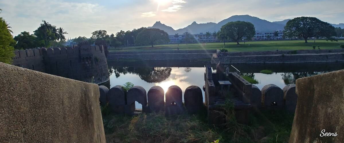 A historic fort with a moat, palm trees, and a mountain in the background.