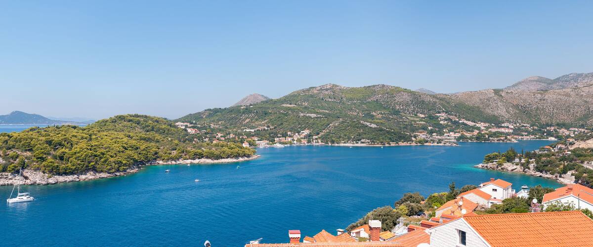 A coastal town with a bay, surrounded by mountains and dense greenery.