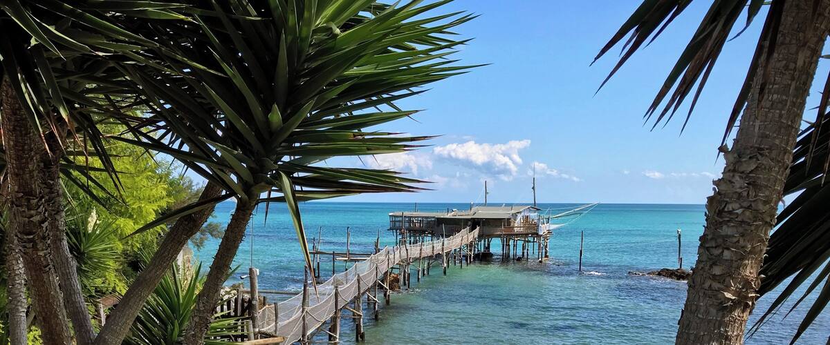 A wooden pier extending into turquoise waters, surrounded by lush greenery and palm trees.