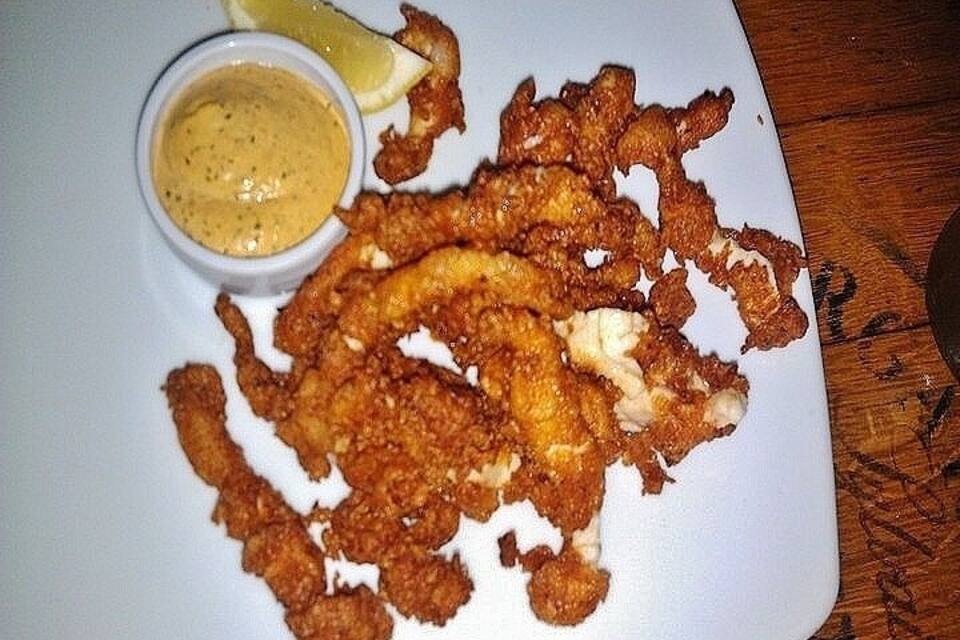 A plate of fried fish with lemon wedges and a side of tartar sauce.