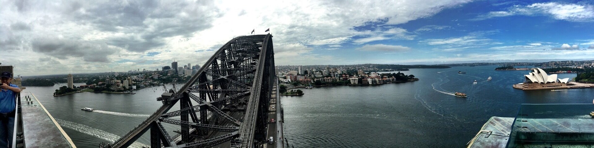 A bridge over a river with a cityscape and a famous opera house in the distance.