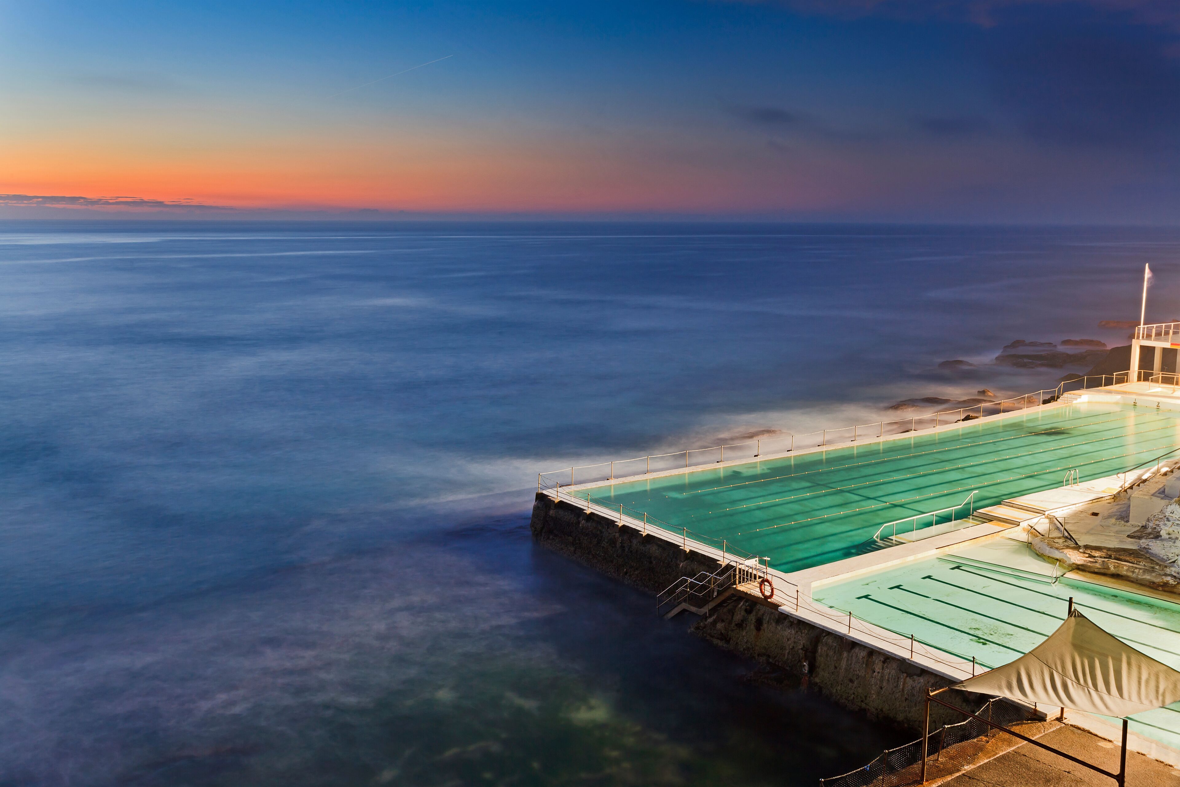 A coastal swimming pool with a view of the ocean and a sunset.