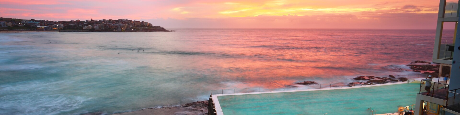 Um pôr do sol costeiro com piscina e edifícios.