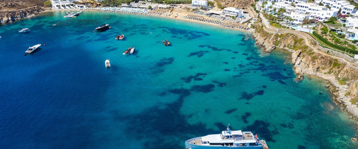 Luftaufnahme des Psarou Strandes auf Mykonos mit türkisem Meer und zahlreichen Luxushotels an der Küste, Kykladen, Griechenland