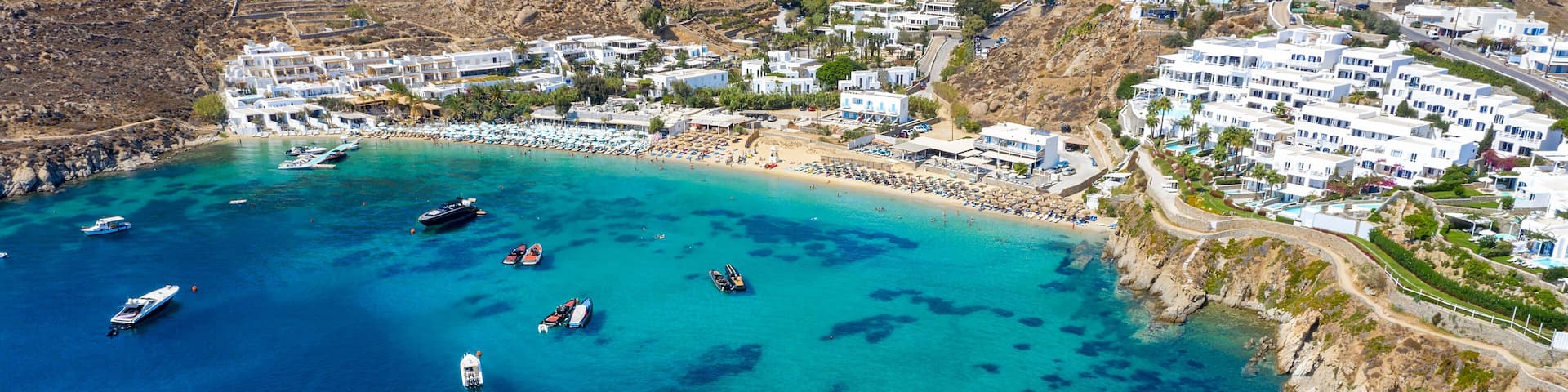 Luftaufnahme des Psarou Strandes auf Mykonos mit türkisem Meer und zahlreichen Luxushotels an der Küste, Kykladen, Griechenland