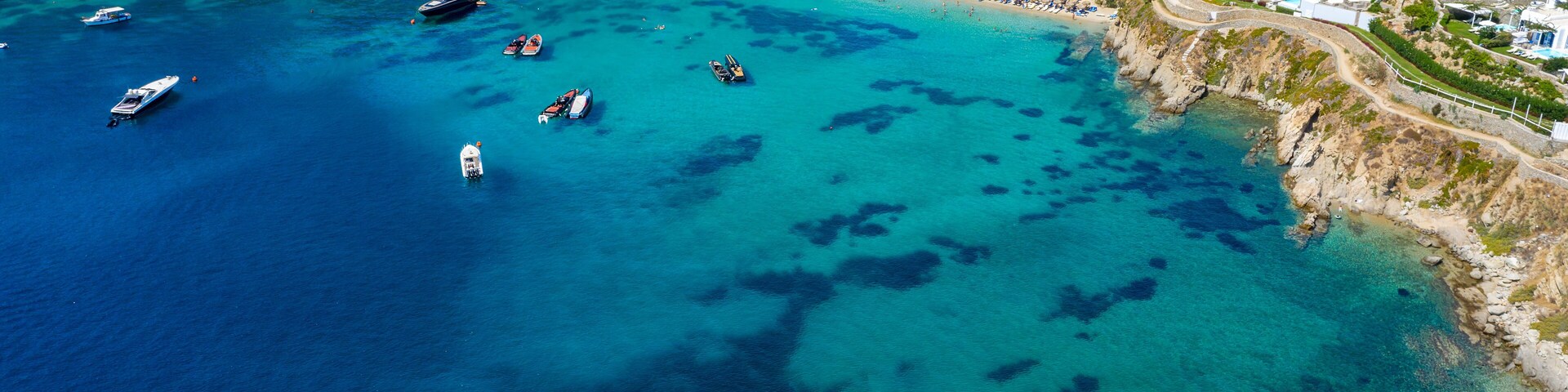Luftaufnahme des Psarou Strandes auf Mykonos mit türkisem Meer und zahlreichen Luxushotels an der Küste, Kykladen, Griechenland