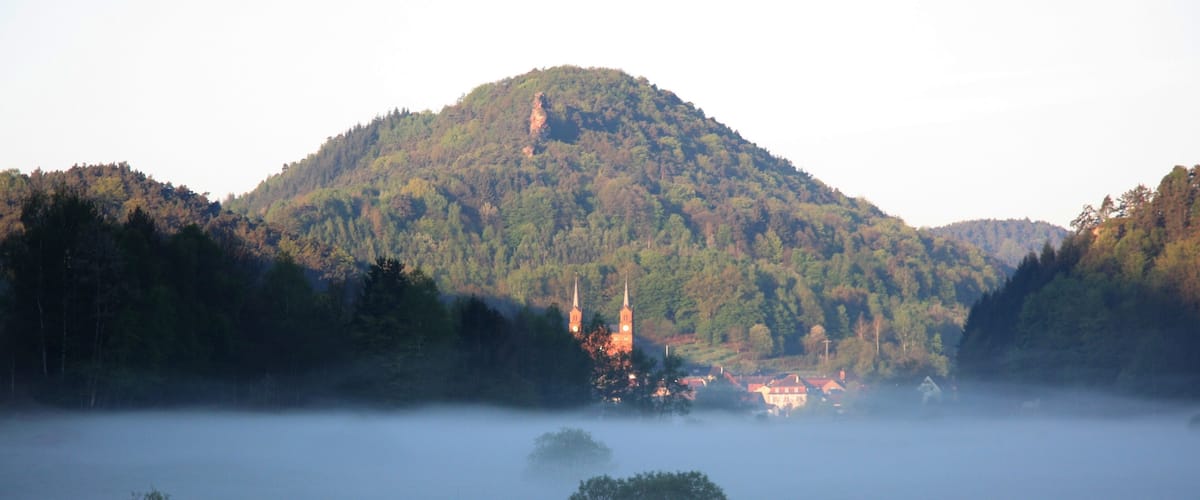 A misty landscape with a church on a hill, surrounded by trees and a foggy valley.
