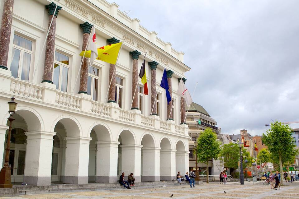 A historic building with multiple flags, including the European Union flag, and a public square with people and trees.