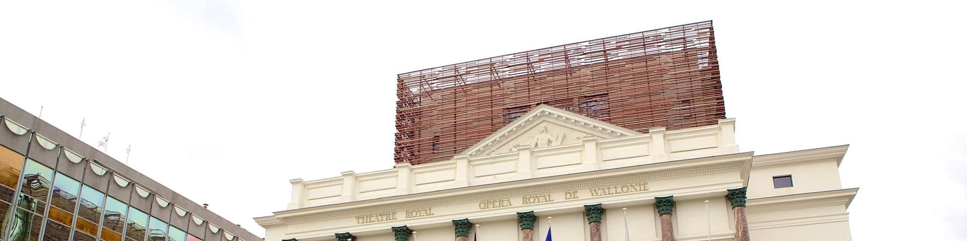 A historic opera house with classical architecture, multiple flags, and a modern building adjacent to it.