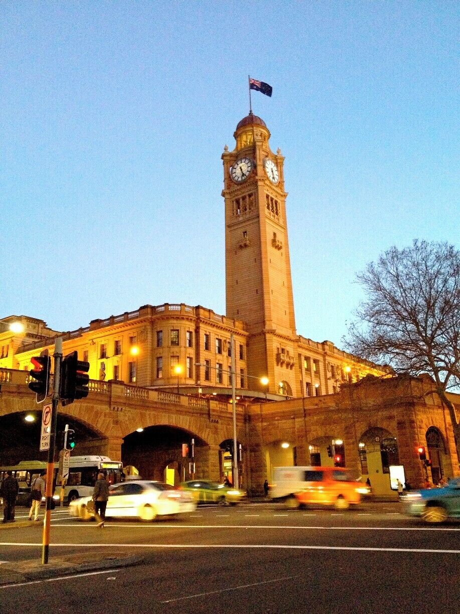 A historic building with a clock tower, a flag on top, and a busy street with cars and pedestrians.