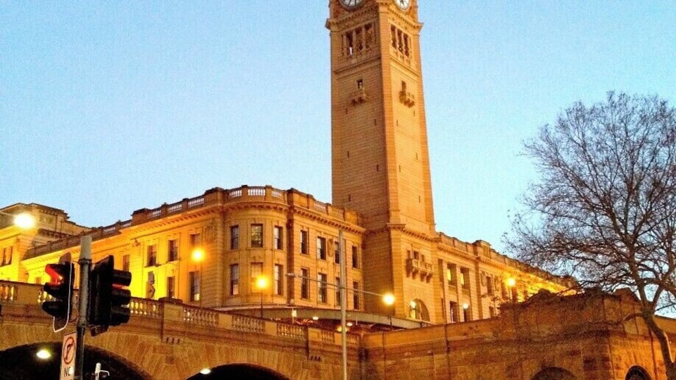 A historic building with a clock tower, a flag on top, and a busy street with cars and pedestrians.