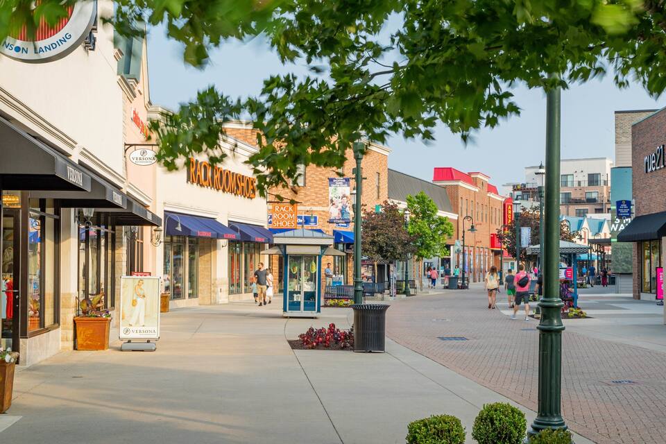 A downtown street with storefronts, including a Rack Room Shoes store, and a bus stop.
