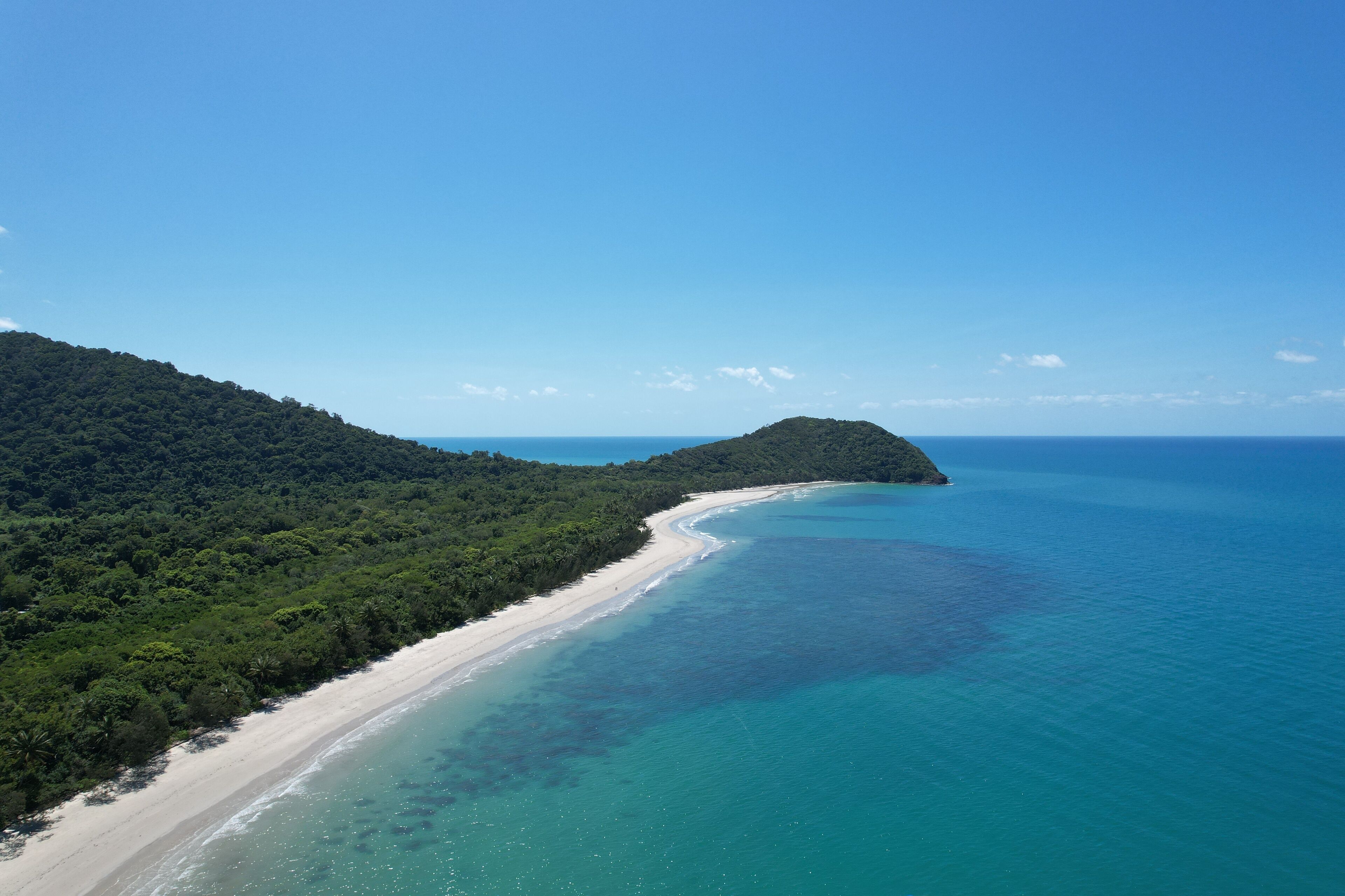 Un paisaje costero con una playa arenosa, aguas turquesas cristalinas y una colina boscosa.