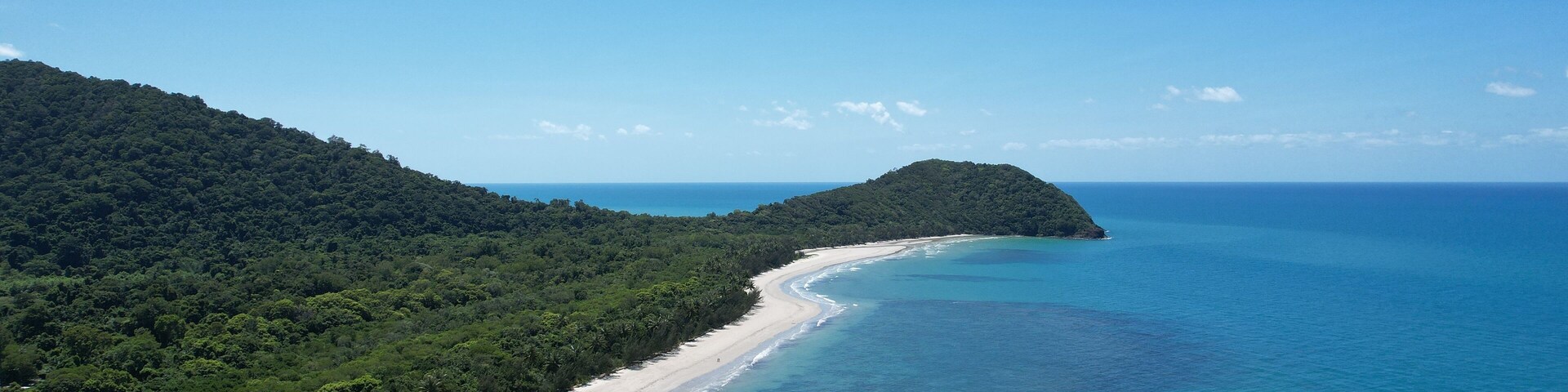 Un paisaje costero con una playa arenosa, aguas turquesas cristalinas y una colina boscosa.