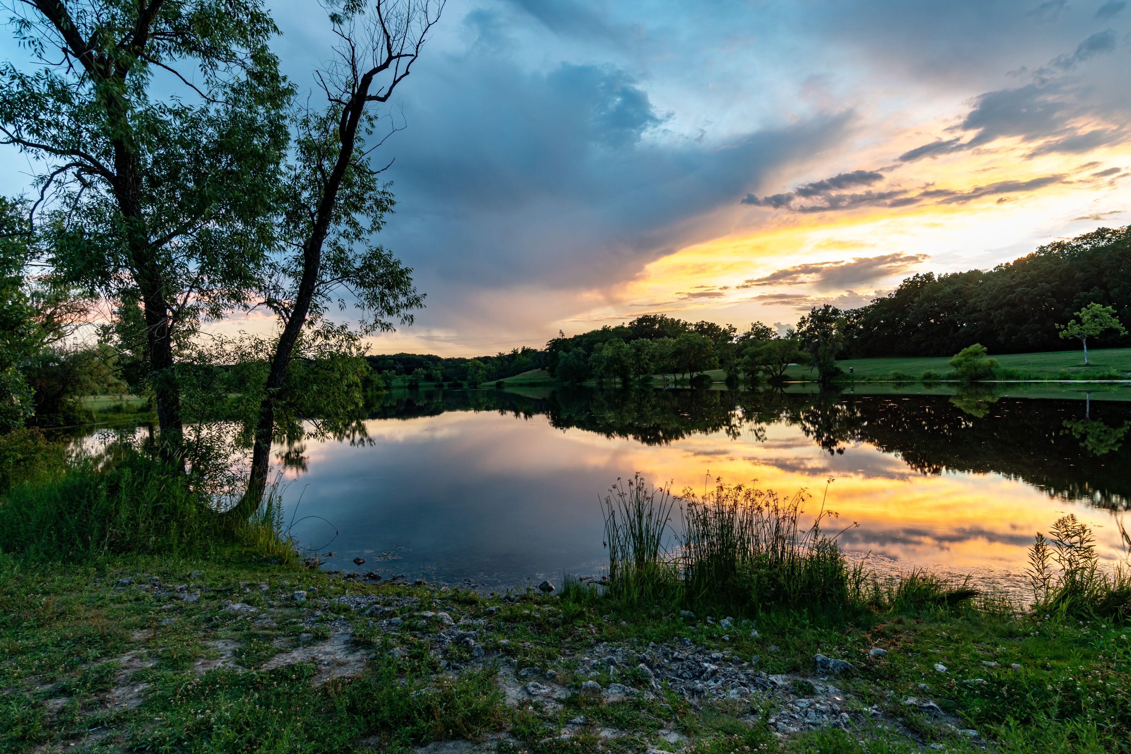 A calm lake reflecting trees and a sunset sky.