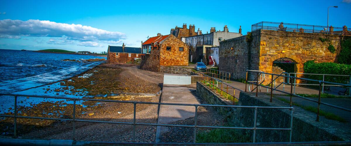 A coastal town with stone buildings, a sea wall, and a clear blue sky.