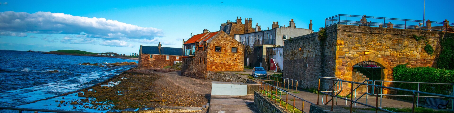 A coastal town with stone buildings, a sea wall, and a clear blue sky.