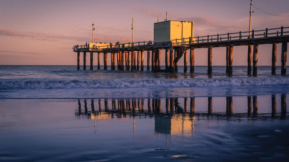 A pier extending into the ocean with a building on it and waves crashing against the shore.