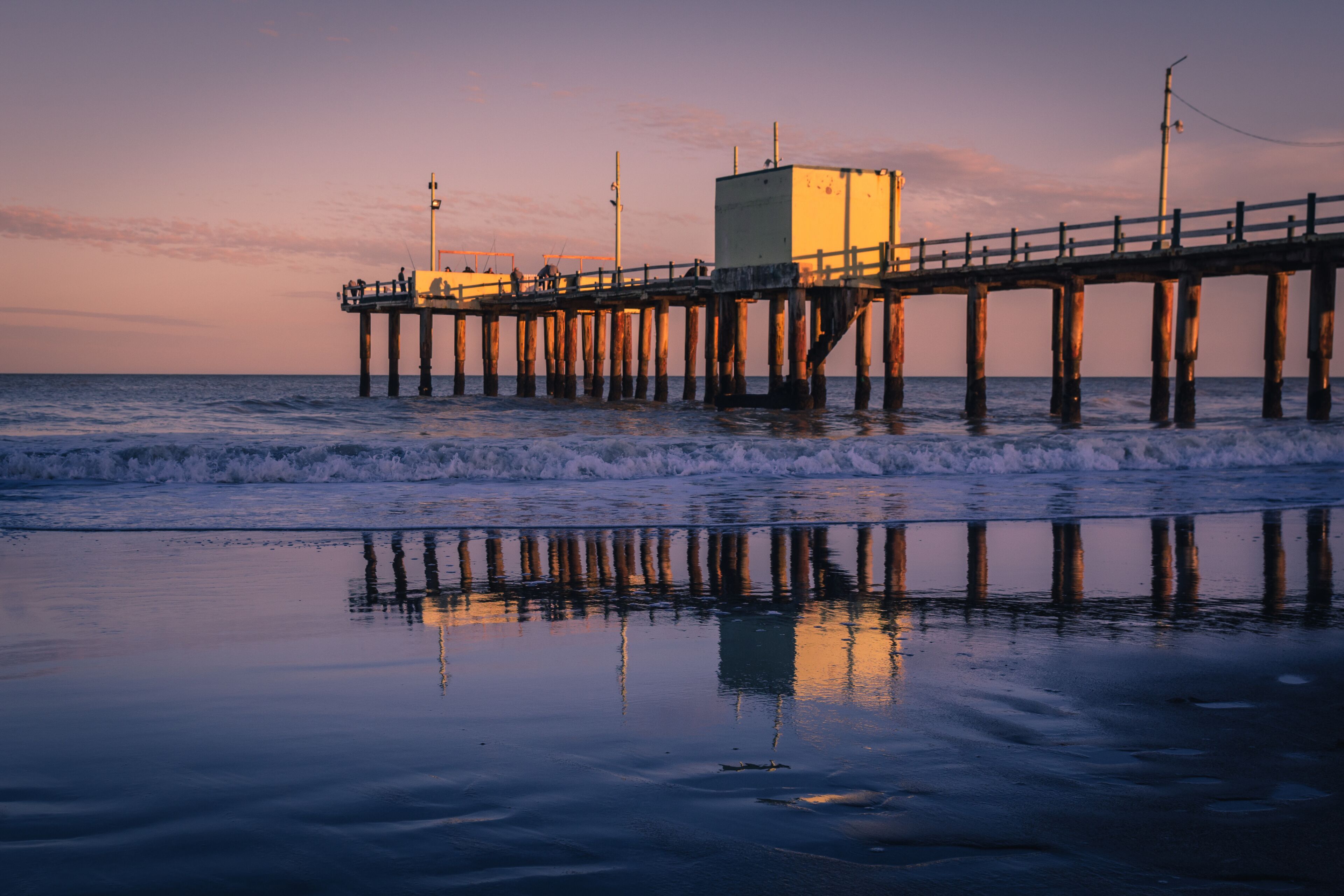 A pier extending into the ocean with a building on it and waves crashing against the shore.
