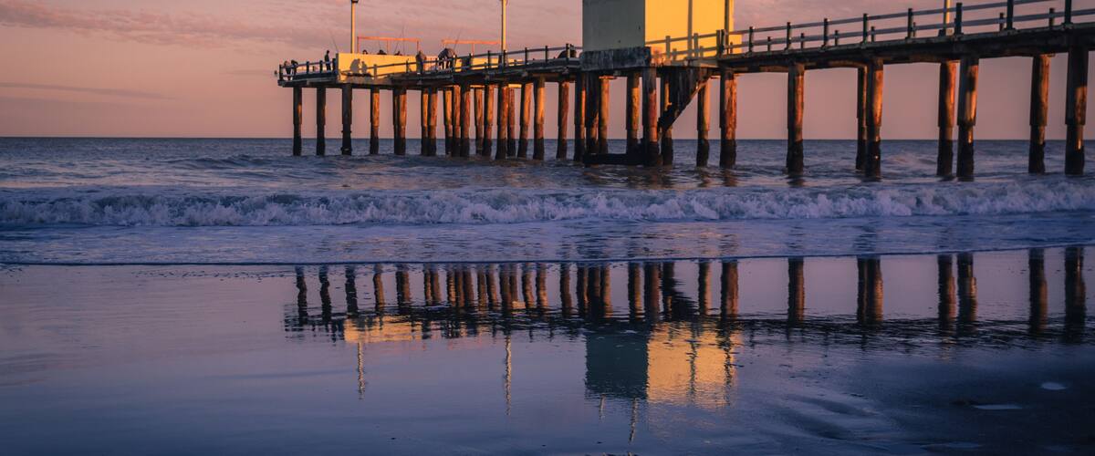 A pier extending into the ocean with a building on it and waves crashing against the shore.