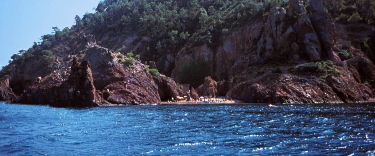 A coastal landscape with rocky cliffs, dense greenery, and a clear blue sea.