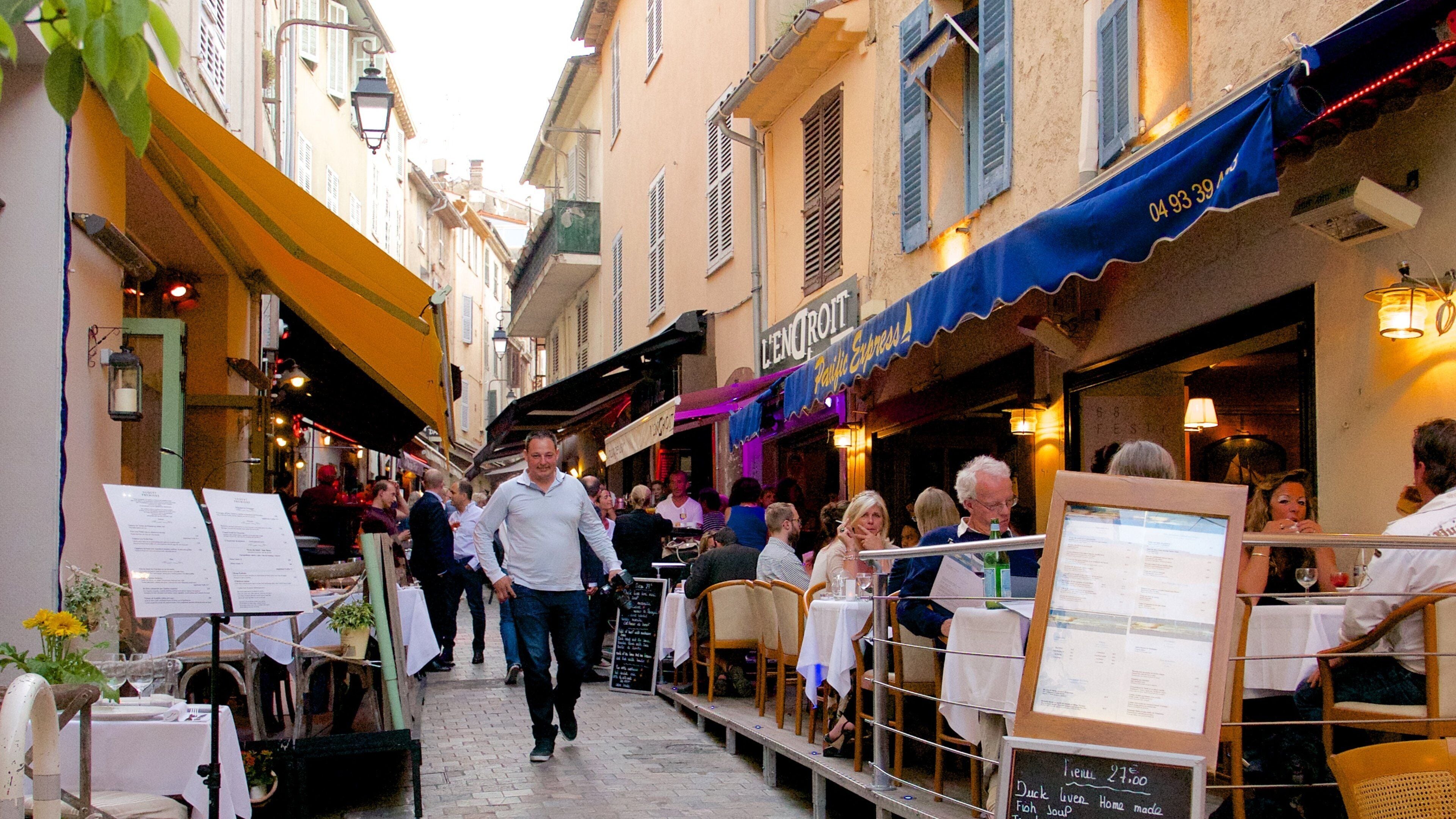 Une rue animée, avec des terrasses de cafés, des passants et un mélange de styles architecturaux.