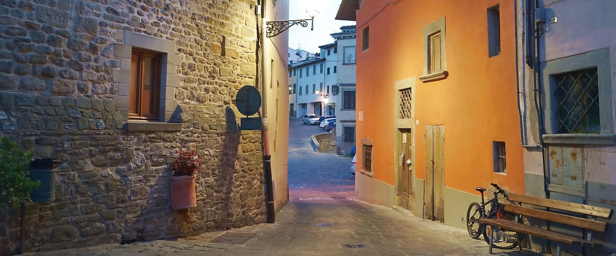 A narrow cobblestone street flanked by stone and brightly painted buildings, with a bicycle and bench in the foreground.