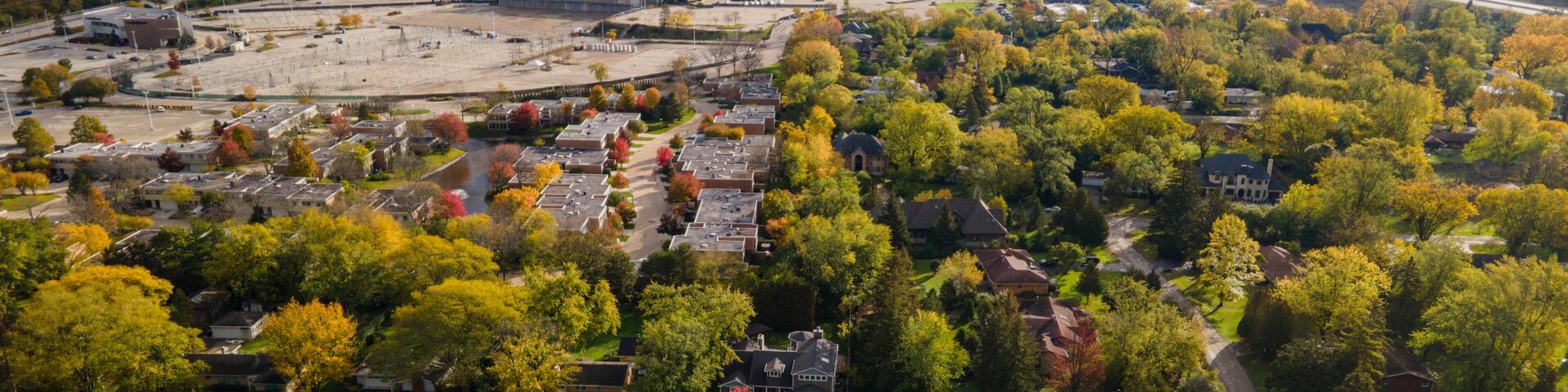 Aerial view of residential neighborhood in Northfield, IL. Lots of trees starting to turn autumn colors. Large residential homes, some with solar panels. Meandering streets