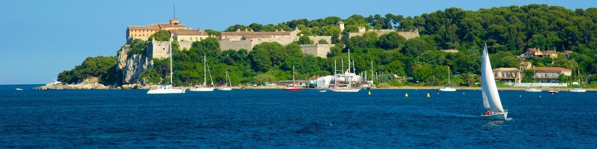 Une ville côtière abritant un château historique perché sur une colline, entouré d’une végétation luxuriante et bordé par une mer d’un bleu limpide.