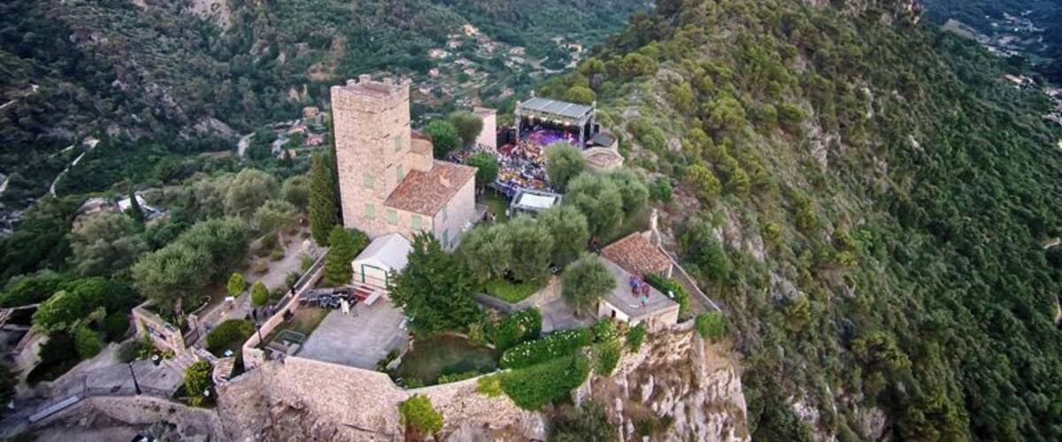 A historic stone tower and ruins on a hillside with a view of a valley and mountains in the background.