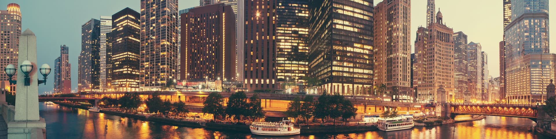 A city skyline with illuminated buildings, a river, and a bridge.