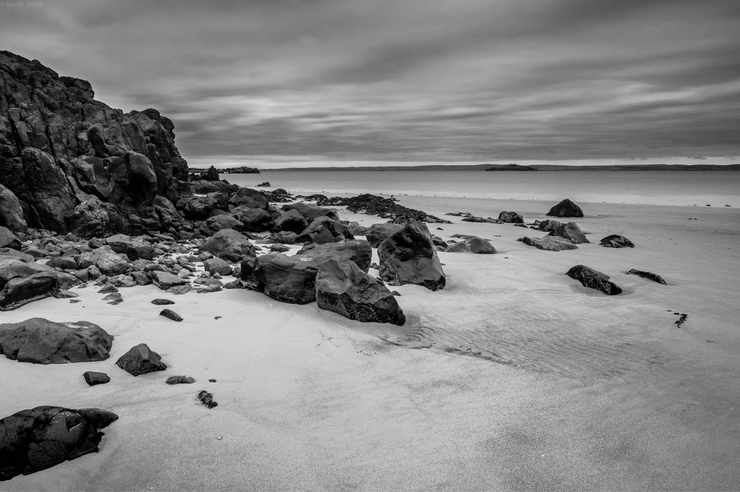 A rocky shoreline with large boulders and a calm sea under a cloudy sky.