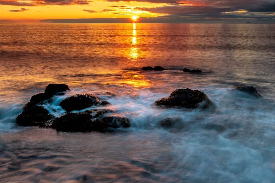 Un atardecer sobre una costa rocosa con olas mansas lamiendo las rocas.
