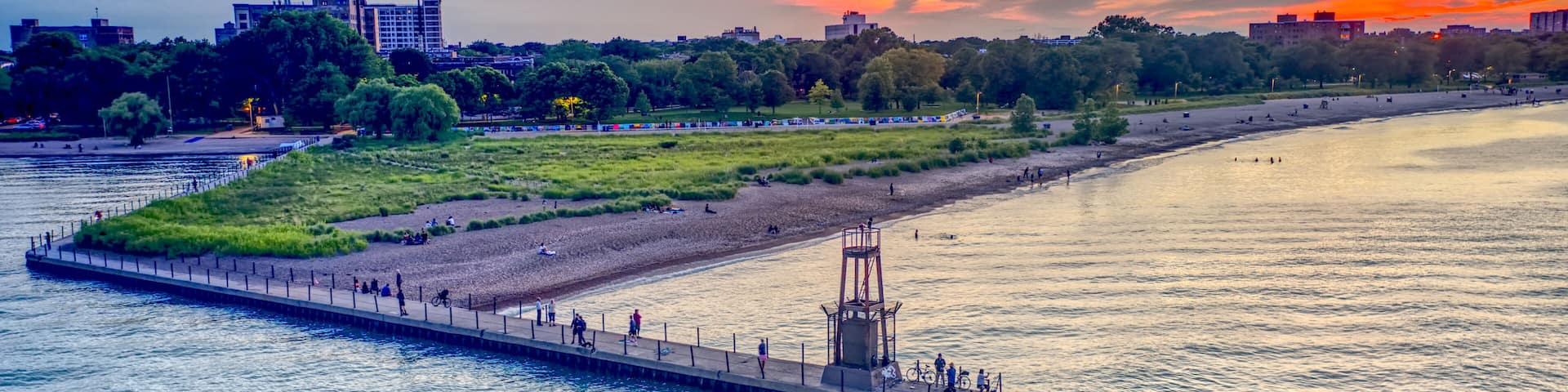 A riverside promenade with a pier, a beach, and a city skyline in the background.