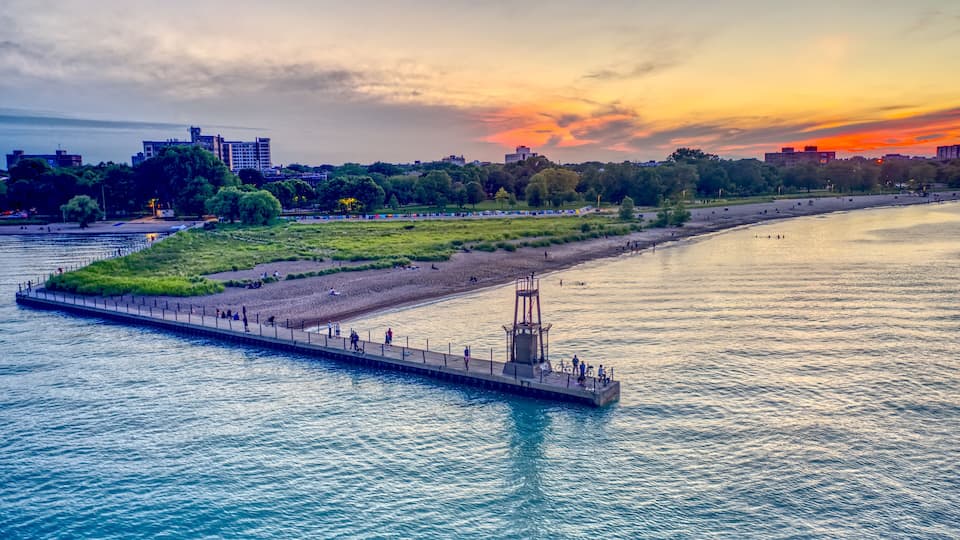 A riverside promenade with a pier, a beach, and a city skyline in the background.