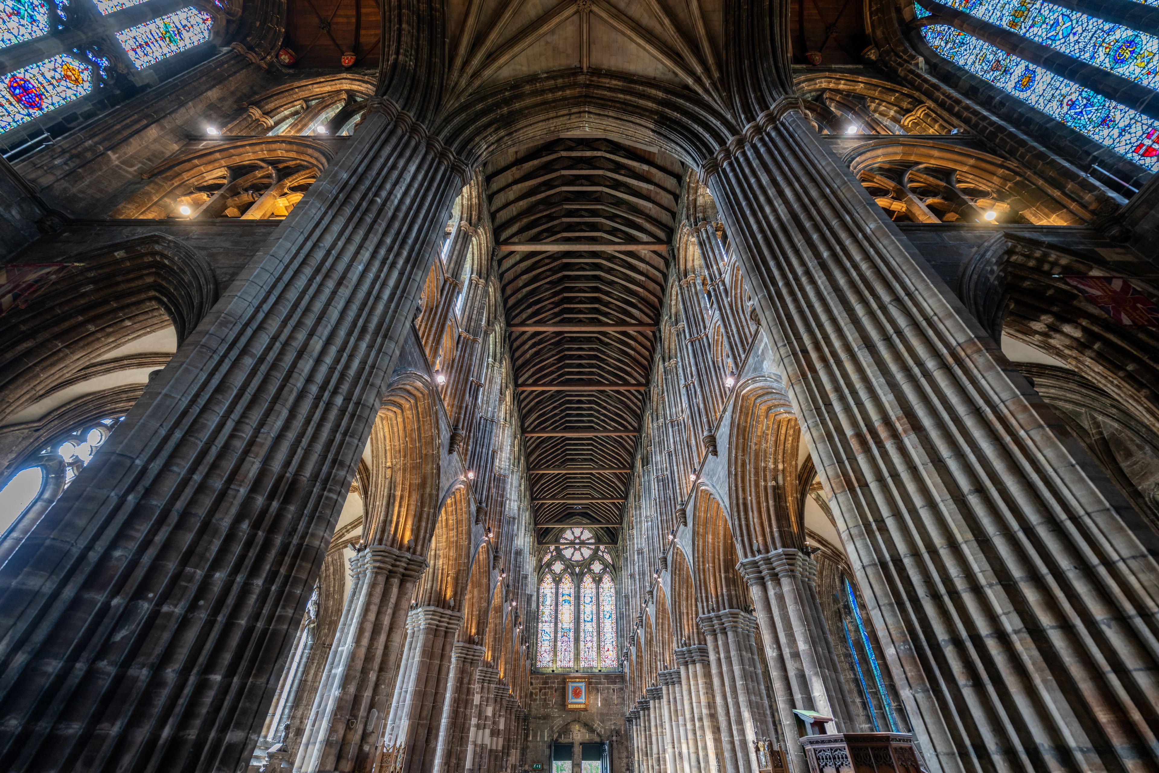 Interior de una catedral con altos pilares de piedra oscura y vidrieras.